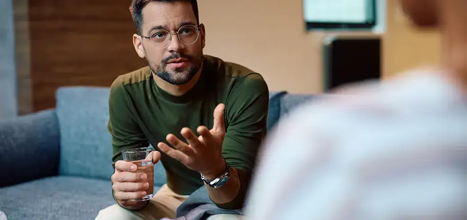 Man holding a glass, speaking with counselor in inpatient rehab session